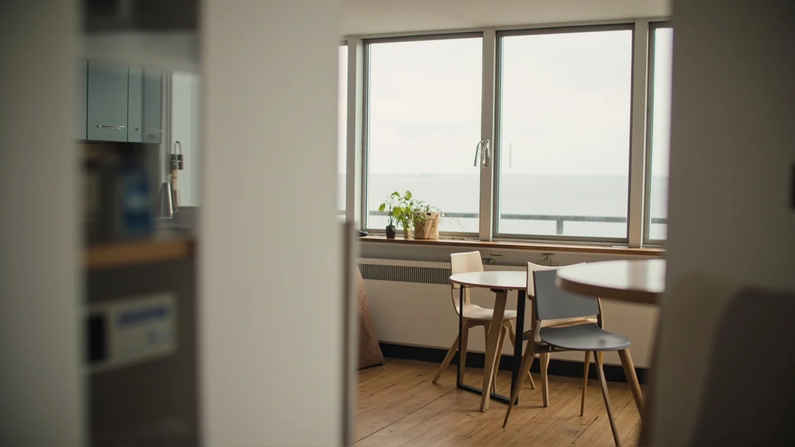 Interior de un apartamento noruego pequeño con cocina, mesa para dos y una ventana con luz de día.
